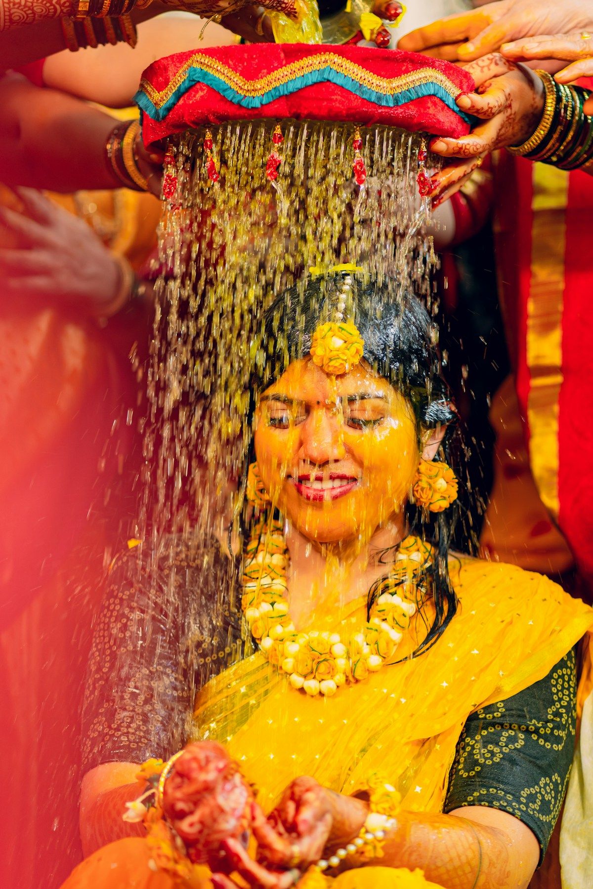 A woman laughing as family pour haldi paste and water over her
