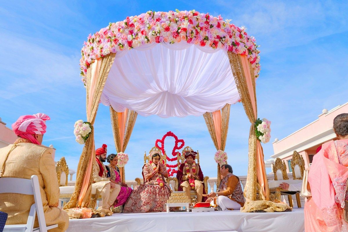 A couple seated under a mandap of pink and white flowers